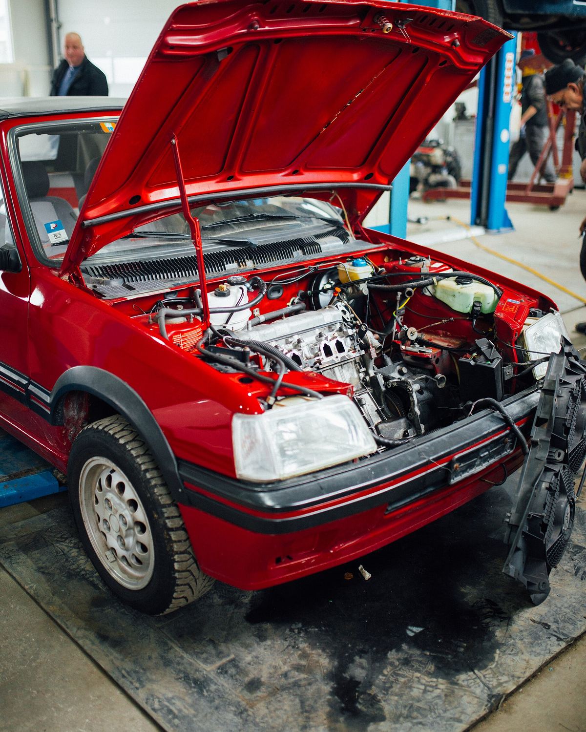 Rode Peugeot 205 met open motorkap in een werkplaats, de motor deels gedemonteerd